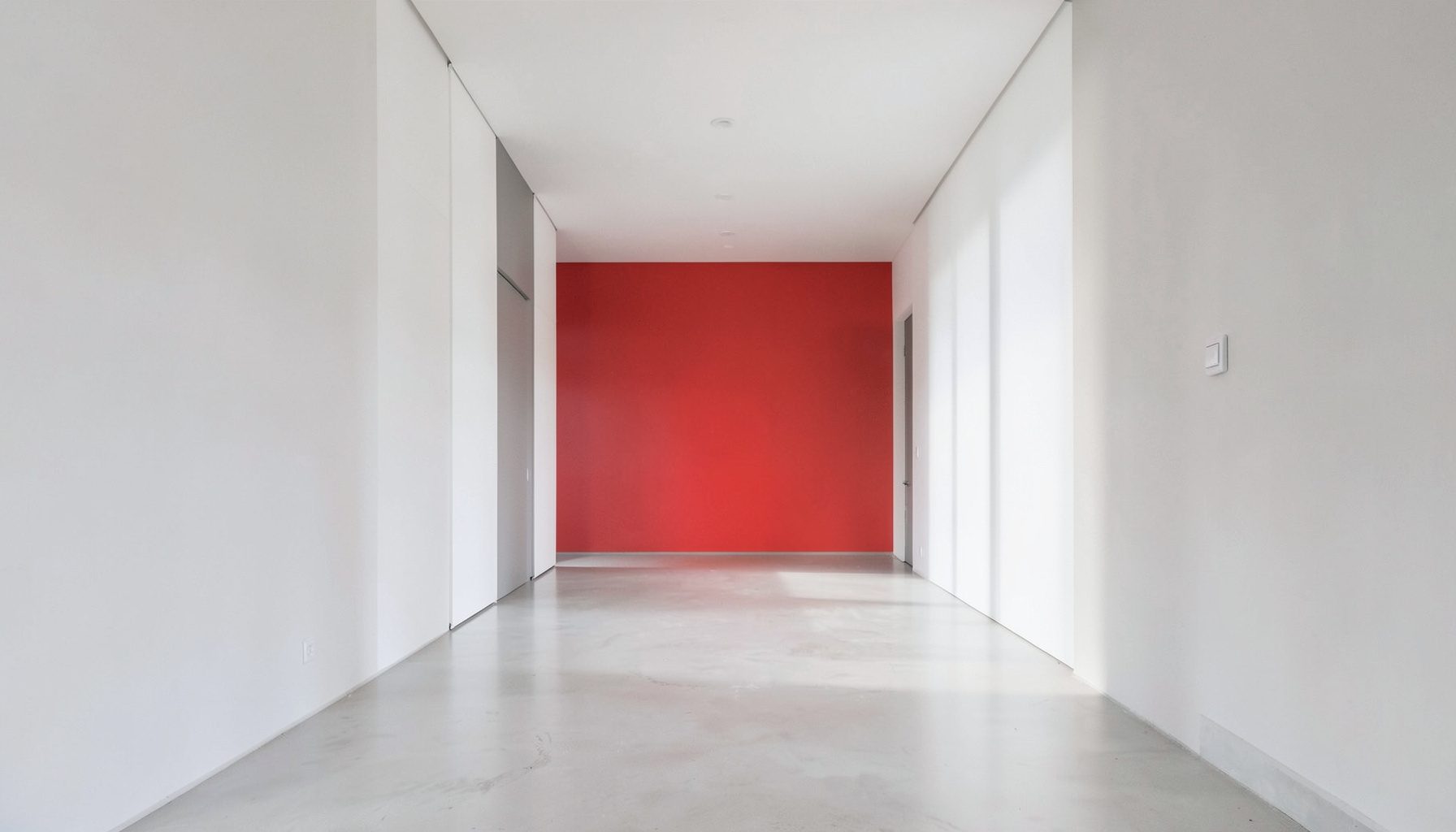 Een rustige, symmetrische architecturale gang met witte en lichtgrijze muren en zacht, kalm daglicht